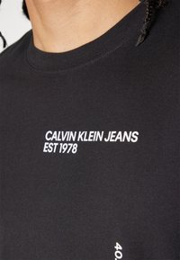 Svart kortärmad t-shirt av mjuk bomull, med vit text "CALVIN KLEIN JEANS EST 1978" och en figurnära rundhalsdesign.