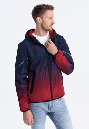 Veste imperméable avec un dégradé de bleu marine à rouge. Dotée d'une capuche, de poches zippées et de poignets élastiques pour un ajustement parfait.