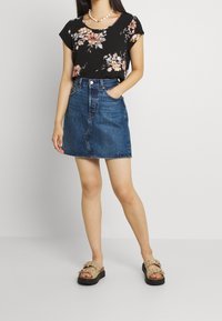 Top negro de flores con mangas cortas, combinado con una falda de mezclilla en corte A. La modelo lleva sandalias beige con detalles. Un atuendo sencillo y casual.