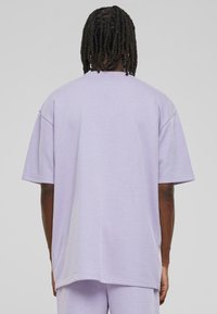 Lavendel Baumwoll-T-Shirt mit gesenkten Schultern und kurzen Ärmeln. Der Rücken hat eine lockere Passform und eine glatte Textur, ohne sichtbare Logos oder Akzente.