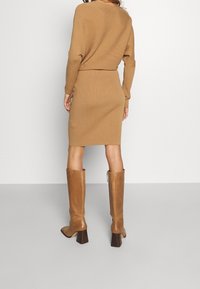 Brun stickad klänning med kroppsnära silhuett, parat med höga bruna klackstövlar. Har långa ärmar och ribbad textur.