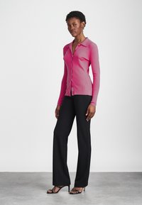 Cardigan rose ajusté à côtes avec un devant boutonné, associé à un pantalon large noir et des sandales à talons noires à lanières.