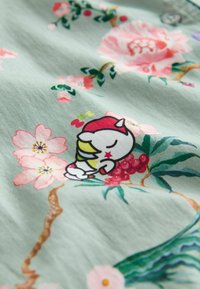 Alvó rajzfilm madár piros sapkában, világoszöld textílián, amelyet rózsaszín virágok, piros bogyók és zöld levelek díszítenek.