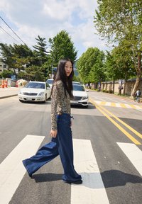 Jeans in denim blu a gamba larga con cintura regolabile, abbinati a una maglietta a maniche lunghe con stampa animale, mentre attraversano un attraversamento pedonale.