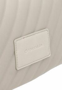Borsa in pelle grigio chiaro con texture trapuntata. Un’etichetta rettangolare con il logo "TOM TAILOR" è attaccata. Finitura liscia con un leggero lucido.