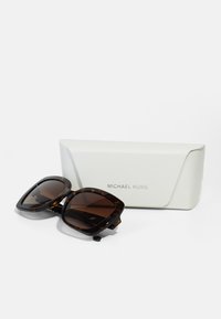 Ochelari de soare tortoiseshell maro cu ramă pătrată, având lentile degradate, pe un toc alb din plastic dur cu logo-ul embosat "MICHAEL KORS".