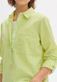 Light green linen shirt with a buttoned placket, single pocket, and rolled sleeves. Textured fabric and a relaxed fit design.