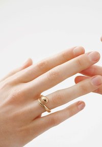 Anillo de oro en un dedo con un diseño de serpiente que presenta escamas texturizadas y un acento esférico liso, sobre un fondo claro.