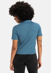 Polo shirt court en bleu sarcelle avec un motif texturé en côtes, doté de manches courtes et d'un col classique, associé à un jean noir taille haute.