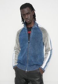 Τζιν μπουφάν με φερμουάρ, σε μπλε και γκρι χρώματα, με ριμπ μανσέτες και πλευρικές ρίγες, που διαθέτει υφασμένο σχέδιο με υφή.