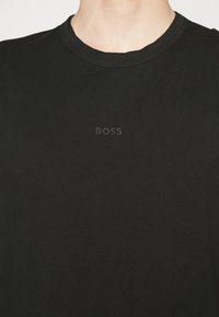 Černé bavlněné tričko s kulatým výstřihem, s jemným tónovým vyšitým logem "BOSS" na hrudi. Hladká textura, volný střih.