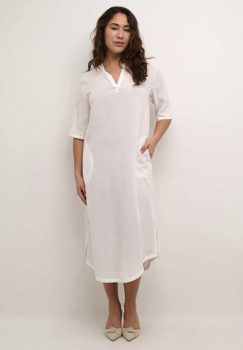 Robe en lin blanc avec un décolleté en V, des manches trois-quarts et deux poches latérales. Présente une coupe décontractée et un ourlet légèrement arrondi.