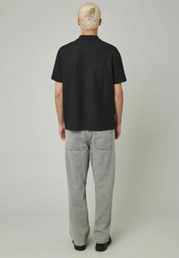 Polo noir à manches courtes avec une coupe décontractée, associé à un pantalon ample gris doté de poches arrière et d'une texture légèrement décolorée.