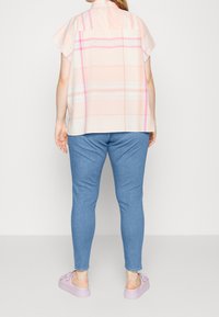 Camisa de cuadros rosa de manga corta con rayas más claras, combinada con jeans ajustados azules y zapatos lavanda, vista desde la parte de atrás.