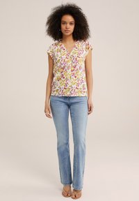 Blusa con motivi floreali su sfondo bianco, scollatura a V e maniche corte arricciate, abbinata a jeans a zampa d'elefante blu chiaro.