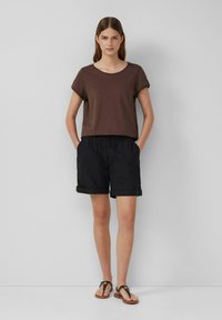 Brązowy T-shirt krótki rękaw, luźny krój; zestawiony z czarnymi szortami do kolan z elastycznym pasem i podwiniętymi mankietami. Czarna klapki.