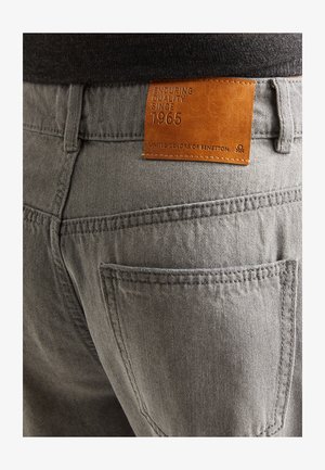 Jeans en denim gris avec une surface texturée, présentant une étiquette en cuir portant la mention "QUALITÉ DURABLE DEPUIS 1965" de United Colors of Benetton.