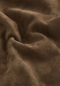 Soft, brown suede fabric with visible texture and natural folds creating light and shadow variations across the surface.