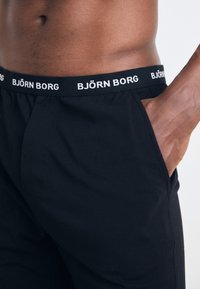 Črne bokserice z elastiko v pasu, na katerih je v belem napisan 'BJÖRN BORG'. Mehka tkanina, stranski žepi in prilegajoč kroj.