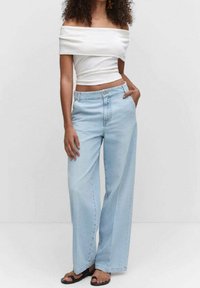 Jeans anchos de mezclilla azul claro, con una cintura de altura media y un corte relajado. Combinados con una blusa blanca sin hombros.