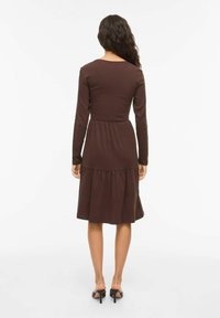 Robe marron à manches longues avec un corsage ajusté et une jupe fluide à volants, en tissu doux, dotée d'un col rond et d'une coupe décontractée.