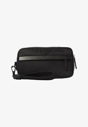 Pochette bracelet rectangulaire noire avec fermeture éclair, bracelet pour poignet, bordure horizontale en cuir et détail de logo métallique centré au-dessus de la bordure.