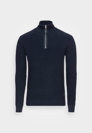 Maglione lavorato a costine di colore blu navy con maniche lunghe, colletto alto e zip frontale in argento parzialmente aperta su uno sfondo semplice.