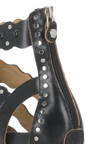 Sandal in pelle nera con ritagli scallopati, borchie argento e dettaglio con zip laterale. Texture liscia e design aperto.