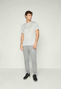Grå bomull t-skjorte med svart Puma-logo, sammen med lyse grå joggebukser med hvit Puma-logo, iført svarte treningssko.