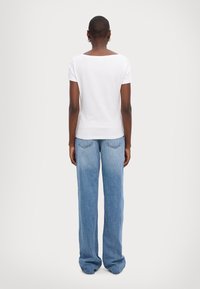 Camiseta blanca de manga corta con escote cuadrado, combinada con jeans de mezclilla sueltos de color azul claro que presentan detalles de costura en los bolsillos traseros.