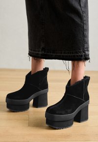 Zwarte suède platform enklaarzen met dikke blokhakken, featuring een opgevouwen manchet en zichtbare stiksels. Geen-slip rubberen zool.