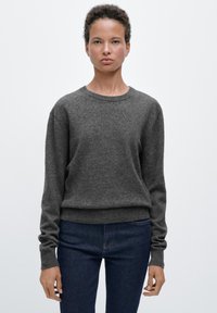 Dunkelgrauer Pullover aus weichem Material mit rundem Ausschnitt, langen Ärmeln und tailliertem Bund. Kombiniert mit dunklen Denim-Jeans.