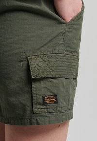 Gröna bomullsshorts med ett texturerat rutmönster, som har en sidoficka och en märkespatch.