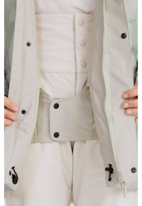 Lightweight jacket in soft beige, featuring a zip closure, snap buttons, and an inner pocket with a contrasting black snap.