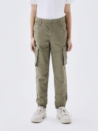 Pantalons cargo kaki avec poches latérales, jambes fuselées et poignets élastiques. Fabriqués à partir d'un tissu léger, associés à des baskets blanches.
