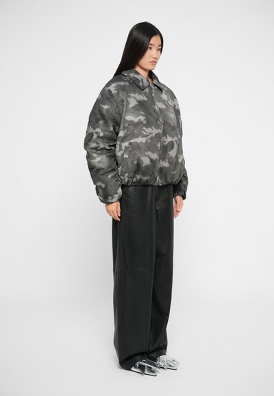 Grijze camouflage bomberjack met een zachte textuur, voorzien van een ritssluiting en geribbelde manchetten, gecombineerd met zwarte wijde broek en metallic schoenen.