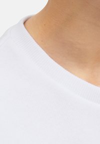 Vitt bomullst-shirt krage, ribbad textur, närbild. Slät tyg med prydlig sömnad, som framhäver hållbarhet och komfort.
