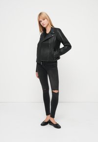 Μαύρο δερμάτινο μπουφάν μοτοσικλετιστή με διαγώνιο φερμουάρ, πλαϊνές τσέπες και μυτερό γιακά. Συνδυασμένο με μαύρο σκισμένο στενό τζιν και επίπεδα παπούτσια.