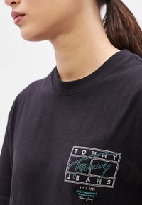 Czarny bawełniany t-shirt z białym logo w konturze z napisem „TOMMY JEANS” i turkusowymi akcentami. Okrągły dekolt i krótkie rękawy.