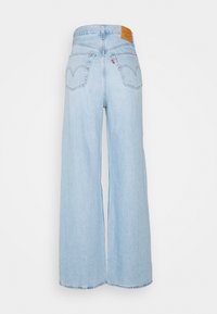 Höga ljusblå vida jeans med bakfickor, bälteöglor och en bruna läderlogotyp på midjan.