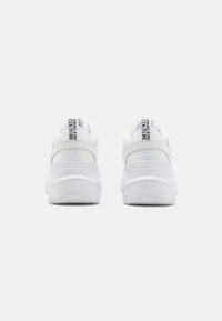 Baskets blanches de sport avec une semelle épaisse, un dessus en cuir lisse avec des accents en textile et un logo de la marque sur la languette du talon.