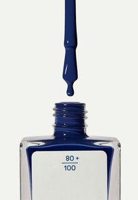 Bouteille ouverte de vernis à ongles bleu foncé avec le pinceau au-dessus et une goutte de vernis tombant vers l'ouverture de la bouteille.