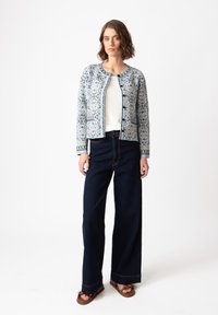 Šviesiai mėlyna raštuota megztinis su puošniais raštais, derinamas su aukštu liemeniu tamsiomis džinsinėmis kelnėmis ir rudos spalvos šlepetėmis.