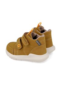 Botas de tobillo de cuero marrón con acentos amarillos, correa de velcro y cuello acolchado. Presentan una suela de goma blanca texturizada para mayor agarre.