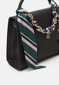 Bolso texturizado negro con un asa de cadena dorada acentuado por una bufanda de rayas verdes y rosas atada alrededor. Presenta un logo dorado en la parte delantera.