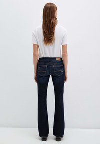 Jeans svasati blu scuro con vita alta, tasche posteriori decorative e cuciture a contrasto, abbinati a una maglietta bianca semplice.