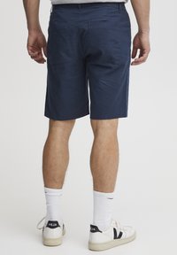 Tmavě modré šortky z měkké látky, se střihem na rovno, dvěma zadními kapsami a bočními švy. Kombinovány s bílými ponožkami a teniskami.