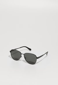 Lunettes de soleil avec monture noire en métal et verres gris, présentant une forme ovale, des branches fines et des plaquettes de nez ajustables. Design minimaliste.