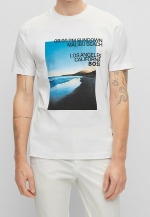 Weißes T-Shirt mit einem grafischen Druck einer Strandszene. Enthält den Text „08:00 PM SUNDOWN MALIBU BEACH“ und „LOS ANGELES CALIFORNIA BOSS“.