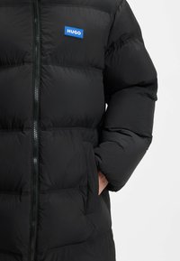 Musta puhvijakki läikikälik finish'iga, seks esiküljel lukuga, küljetaskute ja sinise ristkülikukujulise logo patch'iga rinnal.